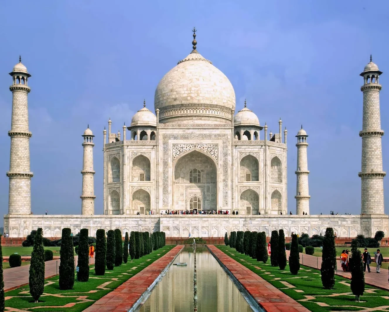 Taj Mahal glowing under a clear blue sky, highlighting its intricate marble architecture and stunning gardens, same day agra