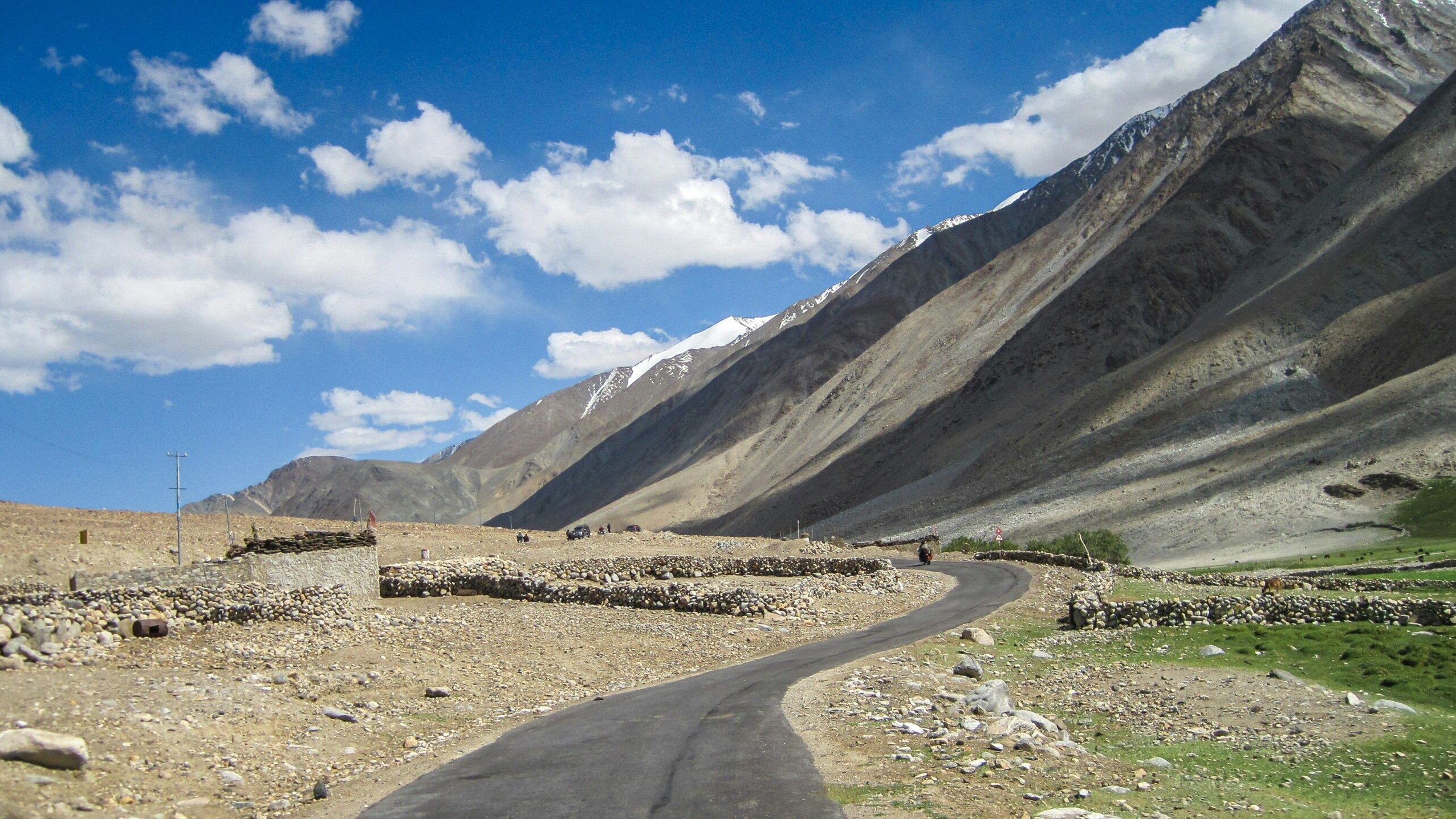 A scenic road winding through the majestic mountains of Leh-Ladakh under a blue sky with fluffy clouds